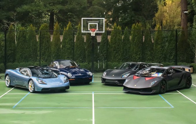 The image shows a group of four luxury sports cars parked next to each other, with one car being a Lamborghini Aventador. The cars are positioned in front of a basketball hoop, suggesting that they might be attending an event or gathering related to both sports and automobiles.
