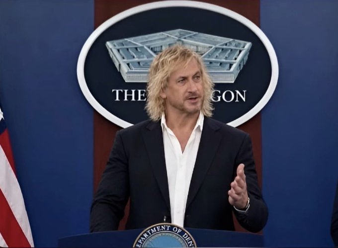 A man with blonde hair speaks at a Pentagon press briefing podium, with "THE PENTAGON" seal and "DEPARTMENT OF DEFENSE" text visible behind him. The image appears to be from a fictional or satirical briefing, matching the post's humorous tone suggesting Iran is close to a significant breakthrough that the U.S. is reportedly monitoring.