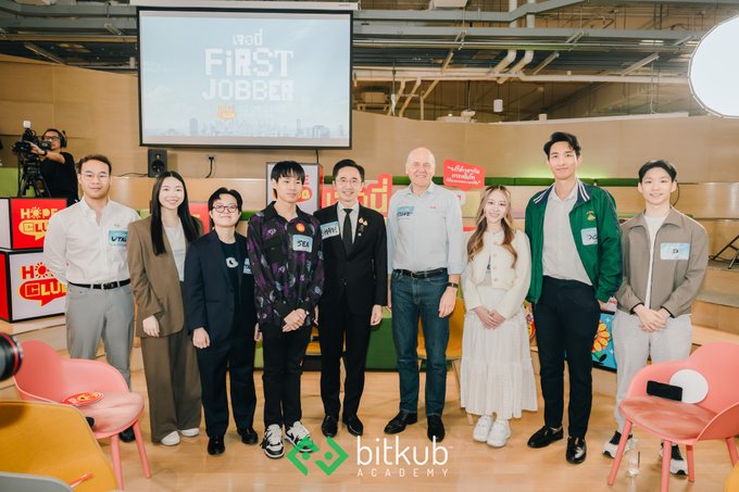A group photo from a 'First Jobber' (first job) event hosted by Bitkub Academy, featuring people wearing name tags including 'VTL', 'TZU', 'SKM', 'SHF', and 'CM' standing in front of a presentation screen.