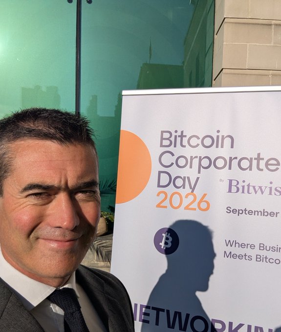 A man in a suit smiles beside a sign for "Bitcoin Corporate Day 2026" by Bitwise, held in September in London, with the visible tagline "Where Business Meets Bitcoin." The image captures him arriving moments before the event's kickoff, as referenced in the post.