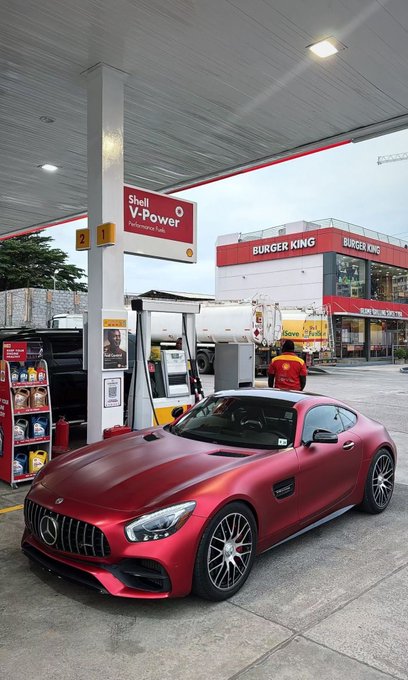 A matte red Mercedes-AMG sports car parked at a Shell V-Power gas station with a Burger King restaurant visible in the background.