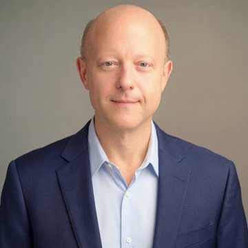 Jeremy Allaire, CEO of Circle, is pictured in a professional headshot wearing a navy blazer over a light blue shirt against a gray background. The image accompanies news coverage of his public defense of Circle's USDC partnerships amid competition from the rival Open USD stablecoin consortium.