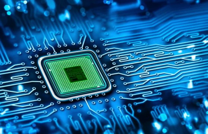 A close-up of a computer chip with a green square center mounted on a blue circuit board with illuminated pathways.