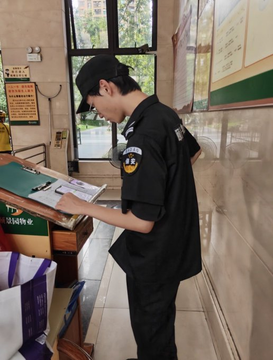 A security guard in a black uniform and cap stands indoors, looking down at a stack of papers resting on a surface in a brightly lit hallway.