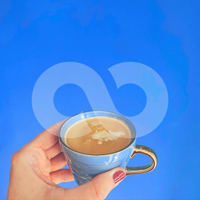 A hand with red nail polish holding an espresso cup against a bright blue background featuring a faint infinity symbol design.