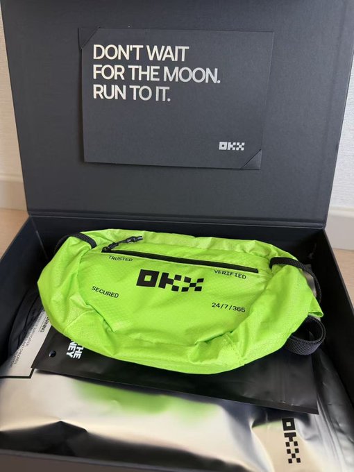 A neon green OKX-branded fanny pack ("TRUSTED," "SECURED," "VERIFIED," "24/7/365") sits inside a black gift box labeled "DON'T WAIT FOR THE MOON. RUN TO IT. OKX," delivered as a Mid-Autumn Festival merchandise surprise from OKX. The bright color of the waist bag reflects the lucky "random" selection mentioned in the accompanying post.