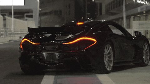 The image features a black sports car driving down a street at night, with its tail lights glowing orange. The car appears to be a luxury vehicle, possibly a Lamborghini or other high-end sports car brand. The car's position on the road suggests that it is in motion and heading towards the camera.
