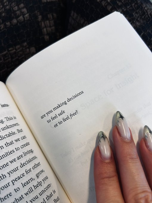 A hand with long, decorated nails rests on an open journal where a page reads 'are you making decisions to feel safe or to feel free?'