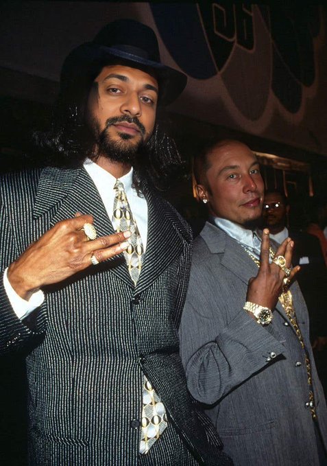 A vintage photograph of two men in suits, one wearing a hat, posing together with elaborate jewelry and rings.