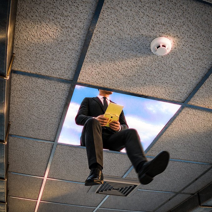 A businessman in a suit reads a yellow folder while appearing to fall or float through a broken office ceiling beneath tiles, a vent, and a smoke detector. The surreal image visually reinforces the post’s message, “There’s no ceiling to your imagination,” by removing the physical ceiling as a barrier to creativity or possibility.