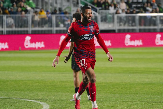 A soccer player wearing a red #37 jersey with "Ford" branding celebrates on the field, with "Chick-fil-A" advertisements visible on the boards behind him. The image ties to the post's reference to the USL Championship, as the player's uniform and setting correspond to a match from that league.