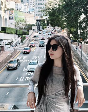 The image features a woman with long hair wearing sunglasses, standing near a busy street filled with cars. She appears to be posing for a photo or waiting at an intersection. The background of the image shows buildings and trees, indicating that she might be in an urban setting. The caption on the post reads "刚从香港回来 终了有空整理相册了 在往前赶的金融气息 两居中确定了没有地址".
