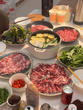 The image shows a table filled with various dishes, including plates of food such as meat and vegetables. There are also several bowls containing different ingredients like tomatoes and other items. The scene appears to be set up for a meal or gathering where people can enjoy the diverse selection of foods available on the table.