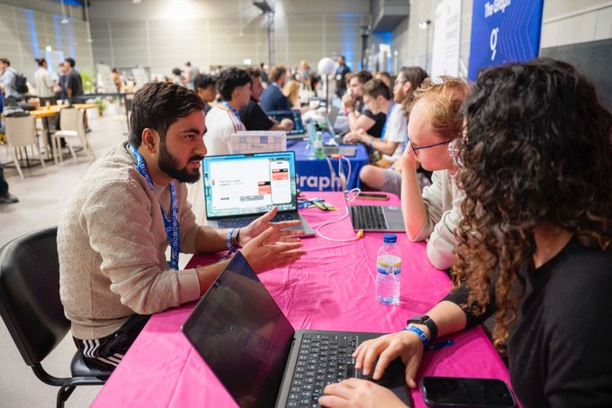 Participants at ETHGlobal Lisbon engage in technical discussions over laptops and drinks during a hackathon event. This scene captures the intense collaborative atmosphere where projects built using the Uniswap API are being reviewed for prizes.