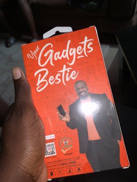 A hand holds an orange "Gadgets Bestie" power bank box featuring a smiling man on the cover, the thoughtful gift referenced in the post for her dad who frequently borrows her power bank, with gratitude given to $GARRI, web3, and @degenBRO__.