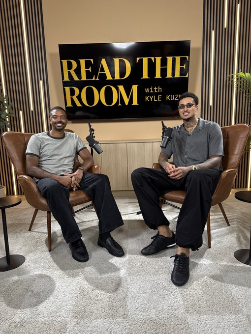 Two men sit in brown leather chairs in a podcast studio setting, with a screen behind them displaying the show title 'READ THE ROOM with KYLE KUZMA'.