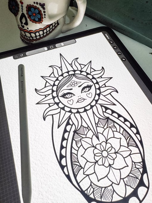A digital drawing of a sun goddess with a decorative flower design on a tablet, accompanied by a stylus and a sugar skull mug.