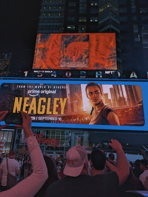 A nighttime city scene featuring large illuminated billboards advertising 'NEAGLEY' on Prime Original, with a crowd of people in the foreground holding up phones.