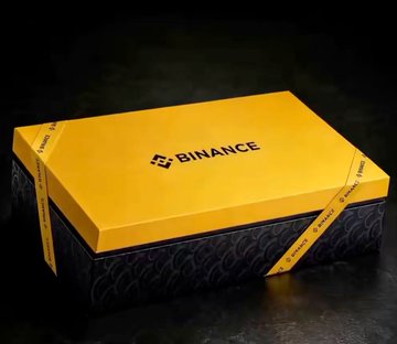 A sleek yellow and black prize-style box branded with the "BINANCE" logo, featured alongside text discussing crypto industry dynamics and a "grand prize." The image symbolizes the allure of cryptocurrency rewards, complementing the post's enthusiasm about Binance-related incentives amid discussion of platform shifts in the crypto community.