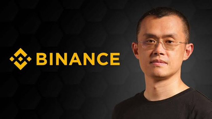 A man with glasses and a black shirt stands next to the Binance logo displayed on a dark background.