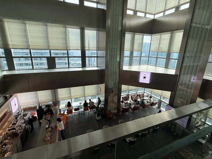 An overhead view of a roadshow presentation at a domestic top-tier brokerage, showing attendees seated in the spacious, glass-walled venue taking photos and engaging with an analyst during a Q&A session on macro topics including the Middle East conflict, Fed rate hikes, and global liquidity.