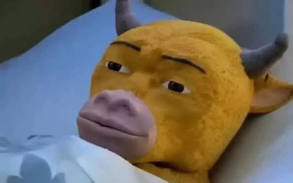 A close-up of a yellow bull cow character (from Shrek) with a tired or skeptical expression, lying down with a blue and white pillow.