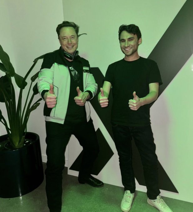 Elon Musk and Nikita Bier, X's Head of Product, pose together giving thumbs up in what appears to be an X office, with a large "X" logo visible on the wall behind them. The image relates to the post about Bier's recent contributions to X since joining as Head of Product on June 30, 2025, including his work on Grok-powered timelines and recommendation algorithms.