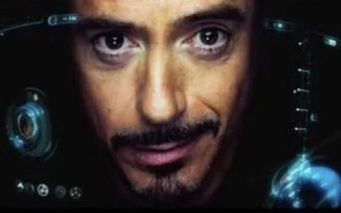 A close-up of Robert Downey Jr. as Tony Stark inside the Iron Man helmet HUD from a Marvel film, with digital interface elements visible around the edges.