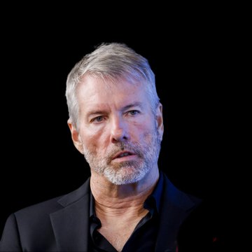 A close-up portrait of a gray-haired man with a beard, appearing serious and contemplative against a dark background, accompanies a quote attributing to Michael Saylor his prediction that Bitcoin will become the world's largest asset within 48 months, with an implied 10x return.