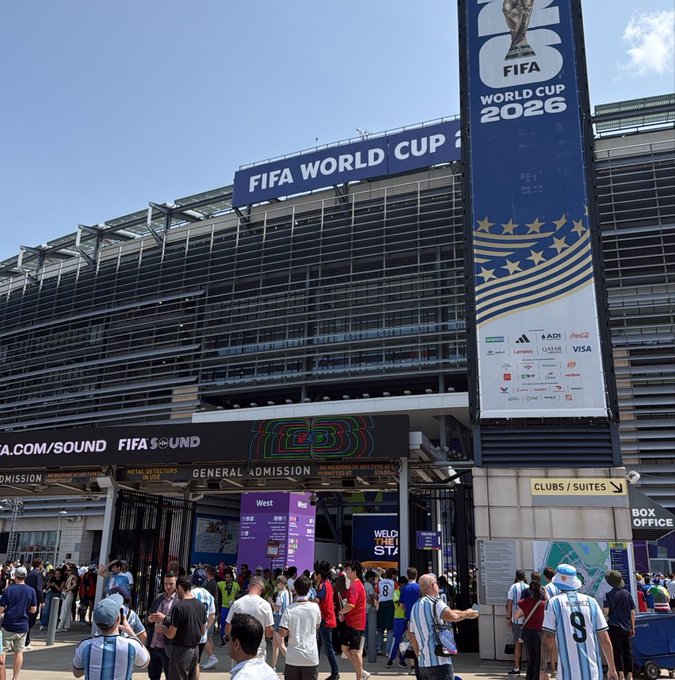 Fans wearing Argentina's light blue and white striped jerseys gather outside MetLife Stadium beneath prominent "FIFA World Cup 2026" banners and FIFA sponsor signage during the final, celebrating Spain's victory. The post expresses gratitude to Binance for the memorable World Cup final experience.