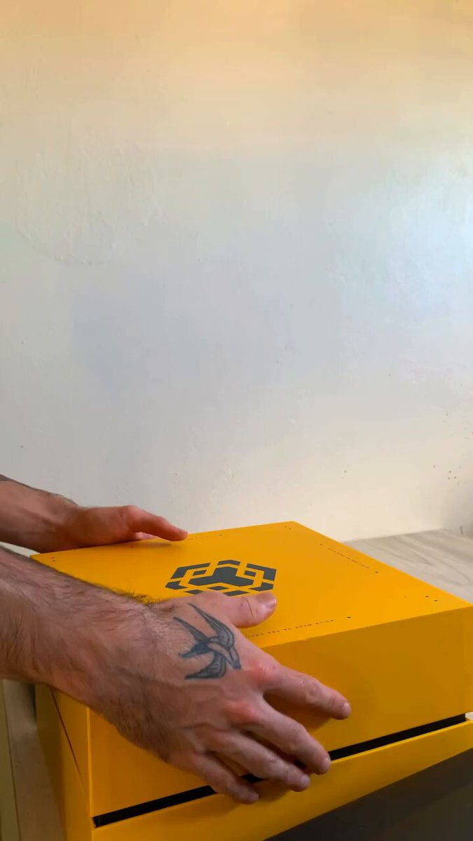 The image shows a person's hand holding a yellow box, possibly containing a new pair of shoes or other items. The background features a white wall, which contrasts nicely with the vibrant yellow color of the box. The caption reads "Thanks @BNBChainLatAm & @BNCHAIN It is an honor to be part of this team and really build with conviction and information". This message emphasizes the importance of teamwork and dedication in achieving success.
