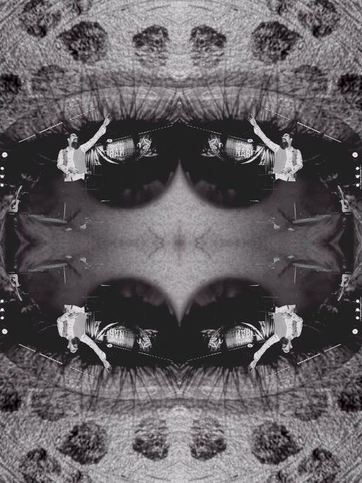 The image features a black and white photograph of a person's face, which appears to be a collage or mosaic with multiple images superimposed onto one another. The faces are arranged in a circular pattern, creating an interesting visual effect that draws attention to the composition. The background is blurred, making it difficult to determine what lies beyond the circle of faces. The image also contains text elements such as "Gm fellas! #ELSEWHERE is finally live. And here’s my participation with @mrbretjolliffe 8/9 Eds 6 $XTZ".