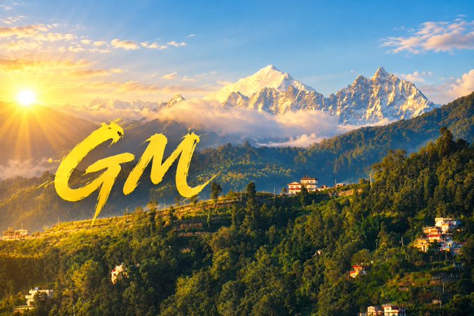 Yellow 'GM' text is overlaid on a scenic view of a sunlit mountain landscape with terraced hills and small buildings.