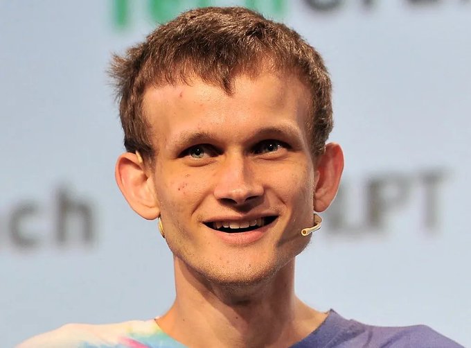 A close-up photograph of Vitalik Buterin, the Ethereum co-founder, speaking at what appears to be a TechCrunch event, wearing a tie-dye shirt and a headset microphone with a colorful background.