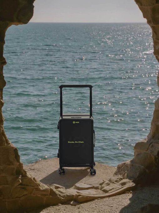 A black portable power station or suitcase-style device with a telescoping handle and wheels sits on stone ground at the edge of a cave opening overlooking the ocean, with text reading 'Stocks, On-Chain.'