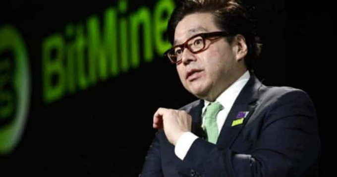 A man in glasses and a suit stands in front of a green 'BitMine' logo backdrop.