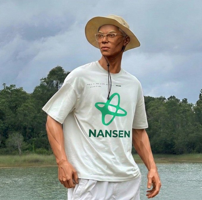 The image features a man wearing a white t-shirt with a green logo that says "Nansen" on it. He is also wearing a hat, sunglasses, and glasses. The man appears to be standing near water or by a lake, possibly at a beach.