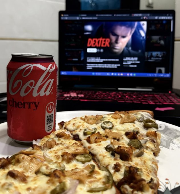 A scene of a pizza, a can of cherry cola, and a laptop displaying the TV show 'Dexter' on its screen.