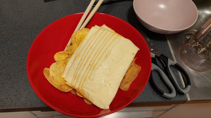 The image shows a plate of food, which appears to be cheese and potato chips, placed on a table or countertop. The plate has been moved from its original position, indicating that someone might have recently rearranged their kitchen or dining area. The photo is captioned with three failed attempts at reclaiming the same zone momentum in the comment section below it.