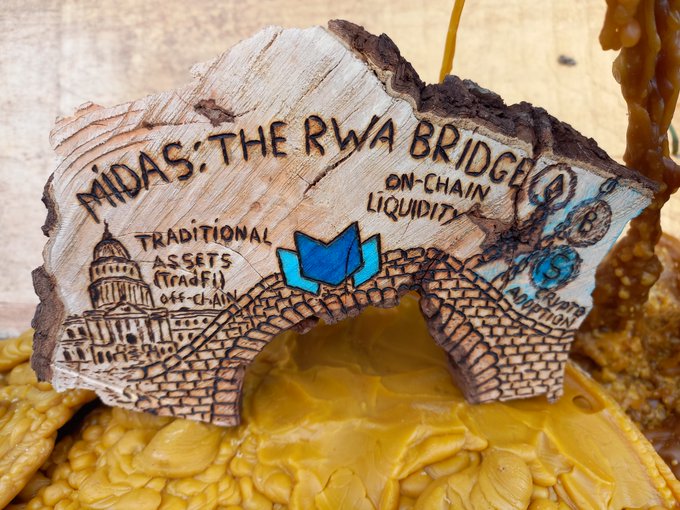 The image features a wooden sign that says "Midas RWA Bridge" written in blue ink, with a picture of a bridge below it. The sign also includes text about digital tokens and real-world stability. The background appears to be a yellowish color, possibly representing a sunset or warm lighting conditions.