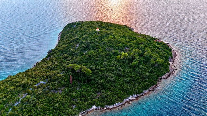 An aerial view of a lush green island surrounded by blue water at sunset.