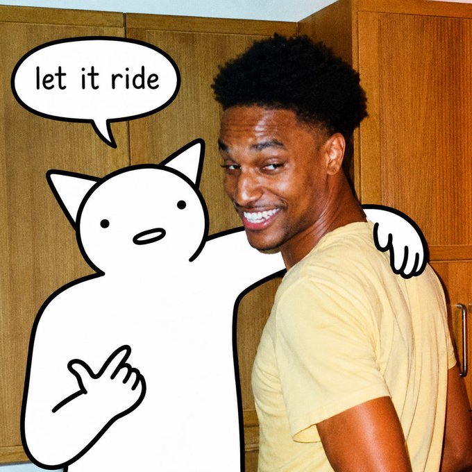 In the image, a man with black hair wearing a yellow shirt stands next to a wooden cabinet. Behind him, there's an illustration of a cat character that says "Let it ride" above his head. The scene appears to be set in a kitchen or dining area where various items are visible, such as a bowl and a cup on the countertop.