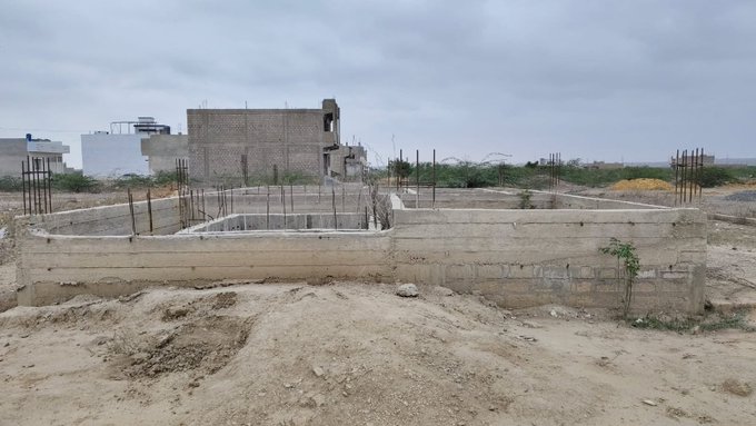 A construction site showing the early foundation stage of a building with concrete blocks and rebar posts, with completed houses visible in the background, reflecting ongoing development. The accompanying post teases an upcoming giveaway to celebrate a significant achievement, suggesting the new construction may be the result of that accomplishment.