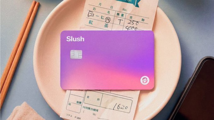 The image features a purple Slush credit card with an electronic signature on top of it, placed on a white plate. The background shows various items such as chopsticks, a cell phone, and some papers. The text "Slush Card is just the first chapter and many more are to follow" suggests that this is part of a series or collection related to the Slush credit card. The post also mentions rewards, referrals, and a smarter way to use funds without cashing out, which could be related to the concept of using the credit card for purchases instead of carrying cash.