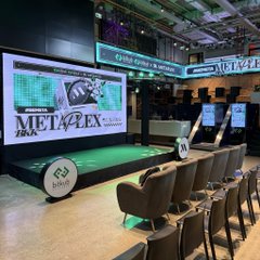 An event space features a stage with a 'METAFLEX' banner and rows of empty chairs facing a presentation setup.