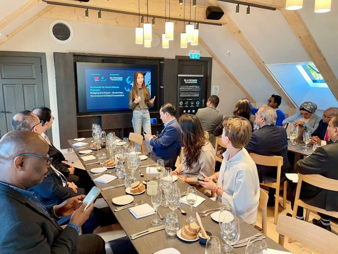 A woman presents at the co-hosted dinner event "Bridging the Future: Blockchain, Governance & Global" with a screen displaying "LingoAI," "Chain for Good," "Singapore IGF," and "United Nations IGF" logos, while seated guests dine and engage with the presentation at the 2025 UN Internet Governance Forum in Oslo.