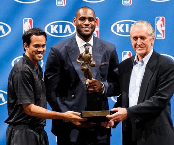 LeBron James holds up his MVP trophy flanked by two coaches at a KIA-sponsored NBA press event. The image evokes memories of his Cleveland stardom as betting odds show him likely to remain with the Cavaliers (44%) over the Heat (30%).