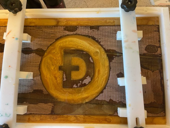 An art piece featuring a metallic/gold P logo on what appears to be a canvas or printing setup with white frame elements and colorful paint splatters.