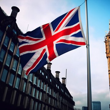 A large Union Jack flag waves prominently against a cloudy sky, set against the backdrop of an ornate British government-style building. The image symbolizes the UK, directly tying to the news about a British court ruling allowing the country to retain $5 billion in seized Bitcoin funds from Chinese fraud victims.