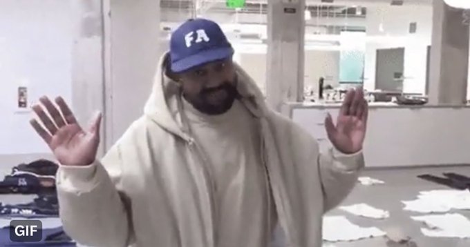 A man with a beard wearing a blue "FA" cap and a beige hoodie stands with his hands raised in a shrug gesture, surrounded by a messy room with clothes scattered on the floor. The image humorously illustrates the post's sentiment of being broke and overwhelmed, as the man's open-handed shrug and the chaotic surroundings visually convey the speaker's frustration about lacking funds to support launching projects.